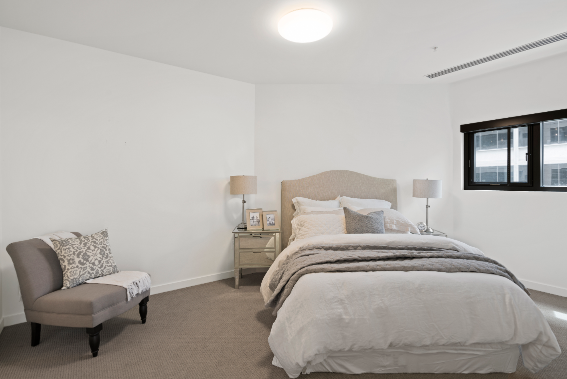 A bedroom with a bed, chair, and nightstand.