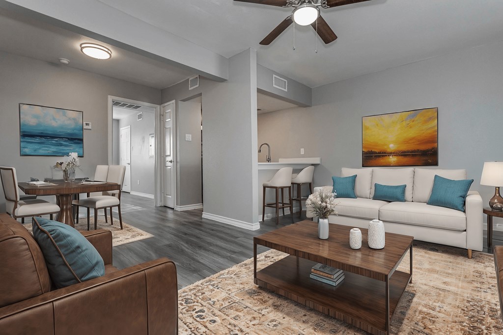A living room with a brown leather couch and a coffee table in front of a painting of a sunset.