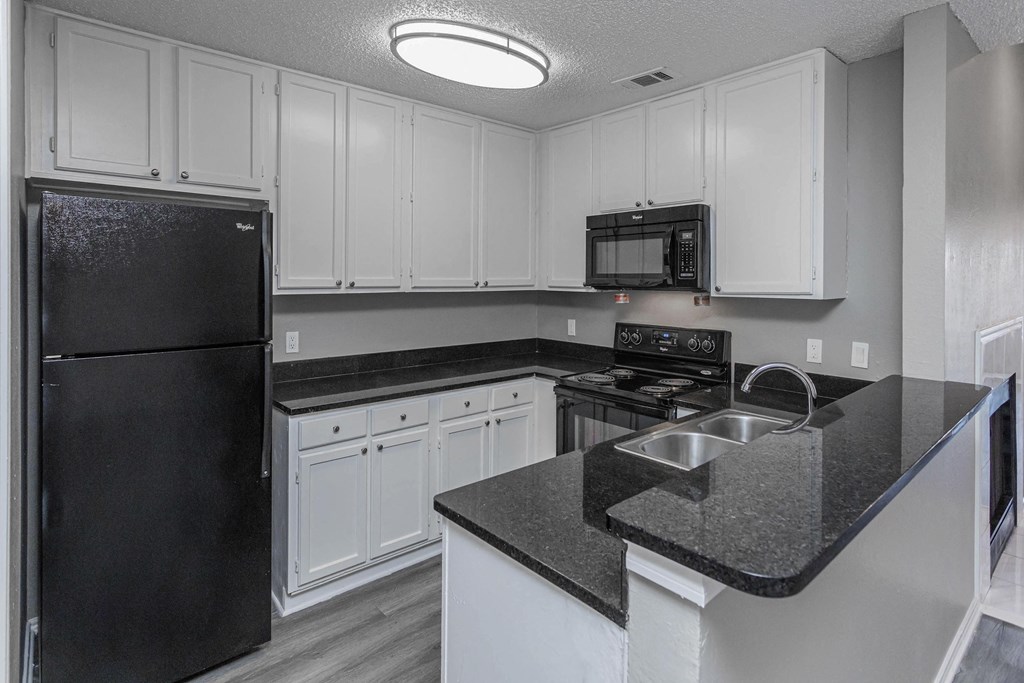 A black refrigerator is in a kitchen with white cabinets.