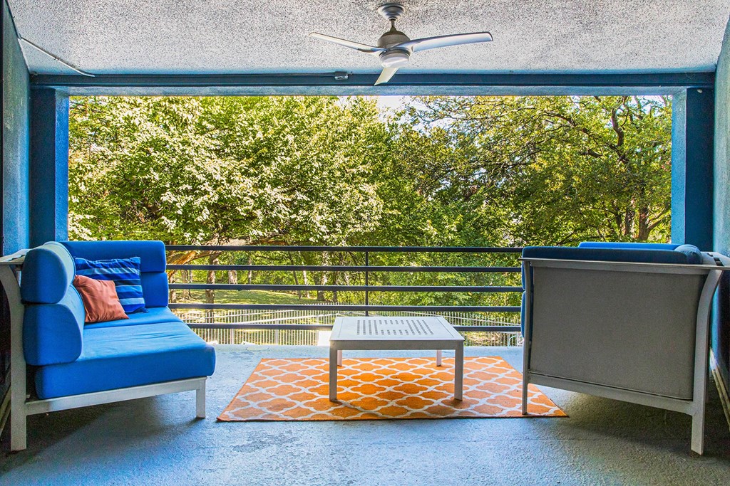 a balcony with a blue couch and a table and a ceiling fan