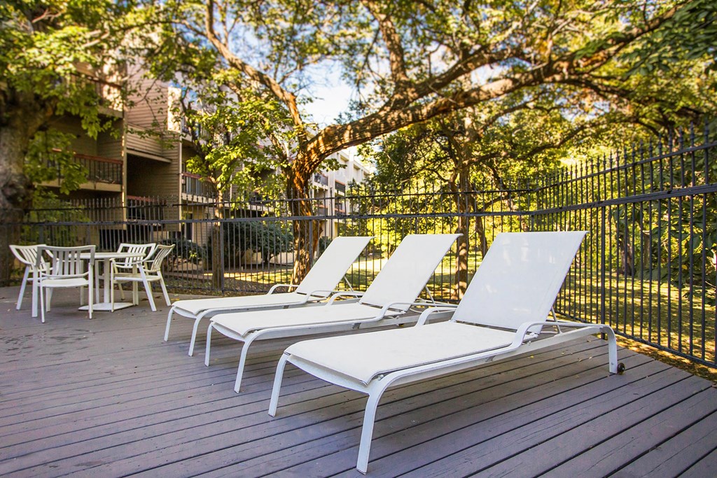 three lounge chairs on a deck in front of a fence and trees