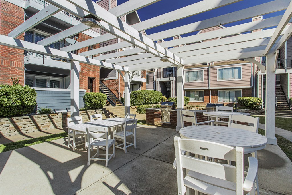 A white patio with a table and chairs under a pergola.