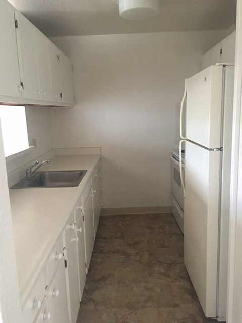 A white kitchen with a sink and a refrigerator.