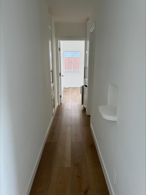 a hallway with wood floors and white walls and a window