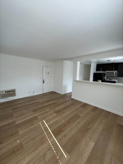 an empty living room with wood flooring and a kitchen