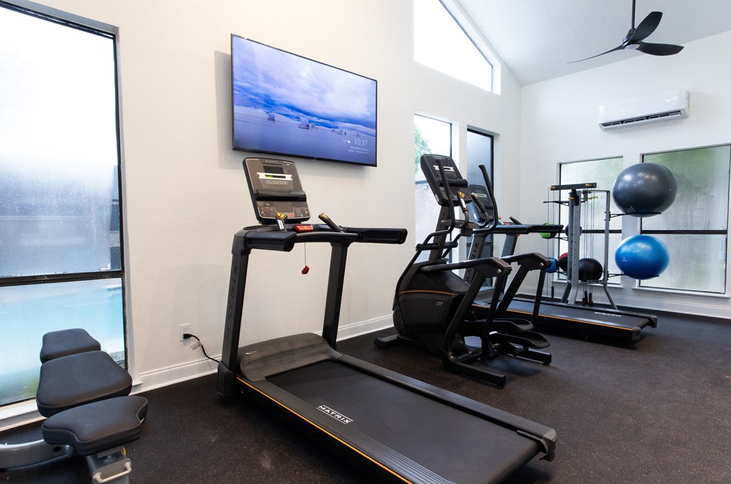 a gym with cardio equipment and a tv on the wall