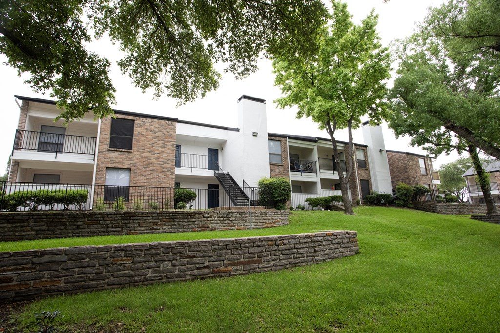 exterior view of apartments with a green lawn and stone retaining wall