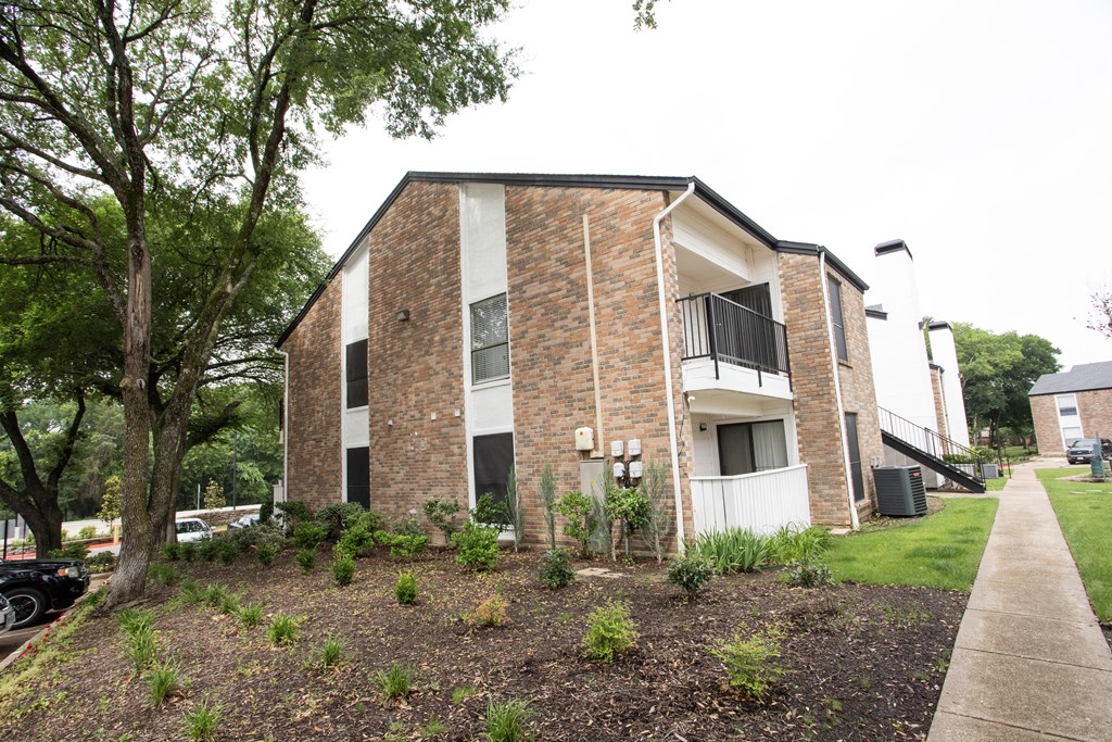 the exterior of an apartment building with a sidewalk and tree