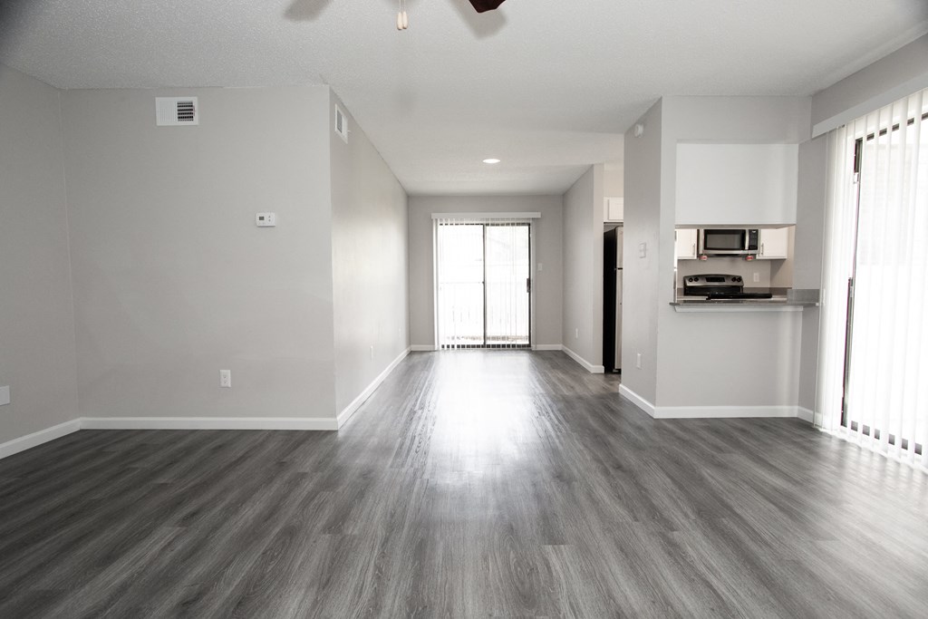 an empty living room with wood floors and a kitchen