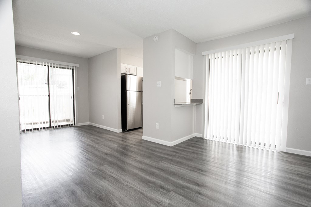 an empty living room with wood floors and a refrigerator
