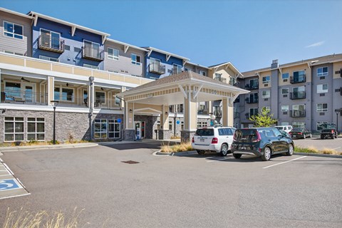 A parking lot in front of apartment buildings with cars parked.