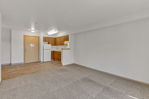 the living room and kitchen of an apartment with white walls and wood flooring