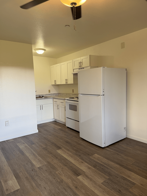 A white refrigerator in a kitchen with wooden floors.