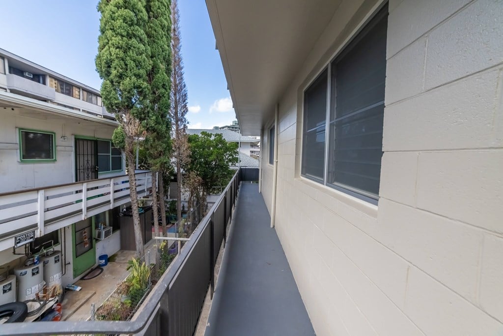 A balcony with a white wall and a tree in the background.