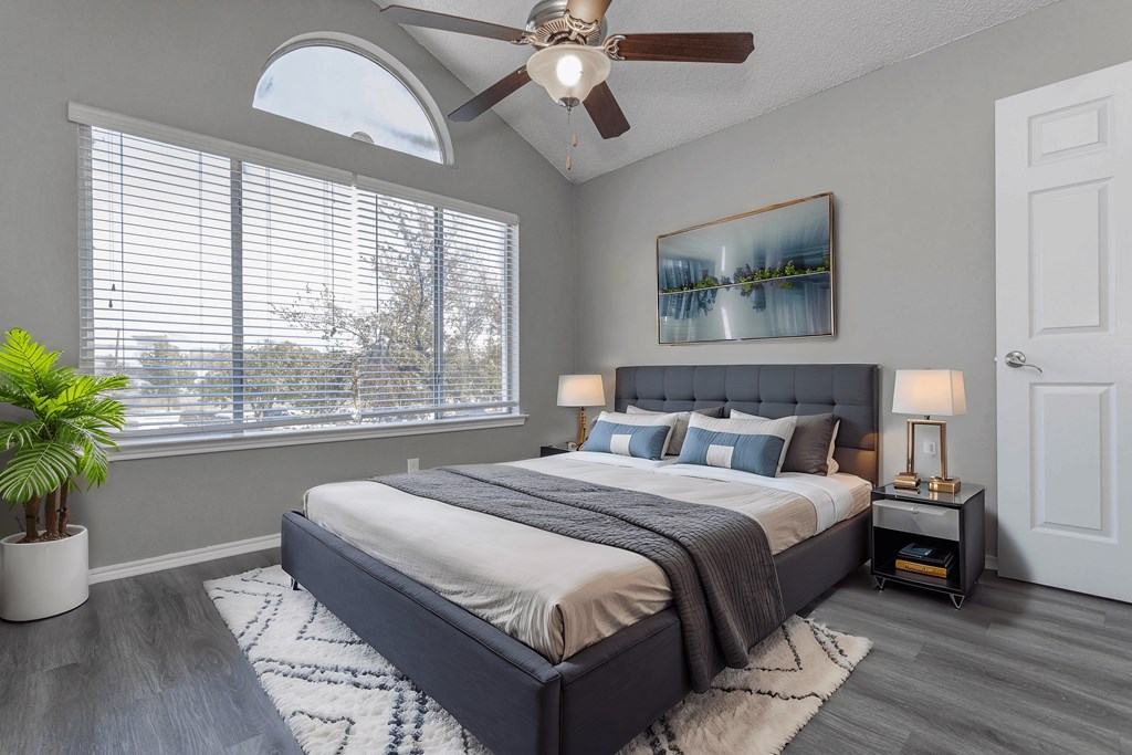 A bedroom with a large bed, a ceiling fan, and a painting on the wall.