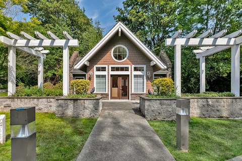 the front of a house with a walkway and two white pergolas