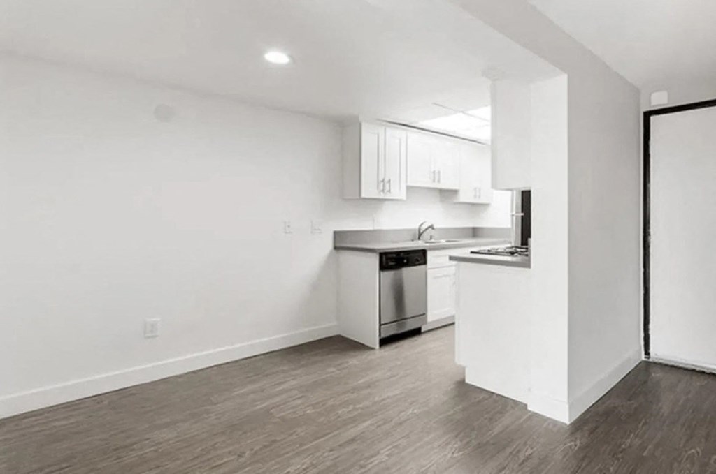 an empty living room and kitchen with white walls and wood floors