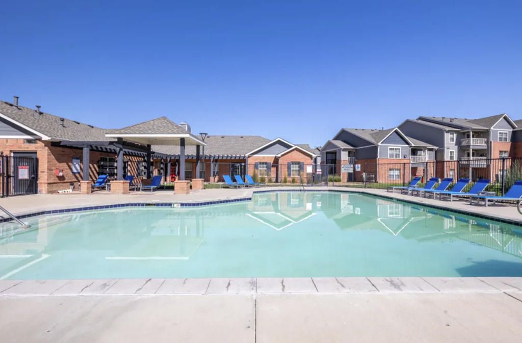 A large swimming pool in front of a building with lounge chairs around it.