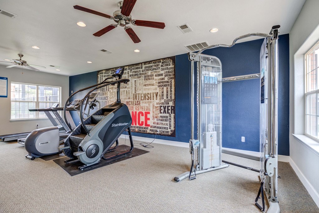 A home gym with a treadmill, elliptical trainer, and a wall with motivational words.