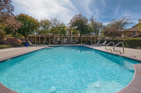 A large outdoor swimming pool surrounded by a fence and trees.