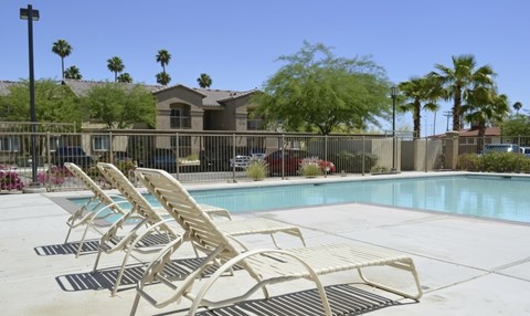 A pool with sun loungers in front of a building with a fence.