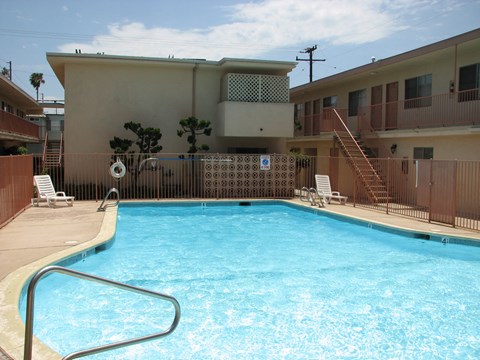A pool in a residential area with a brown fence and a building in the background.