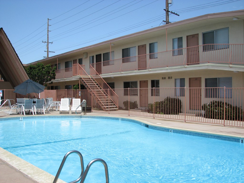 A pool in front of a building with a balcony.