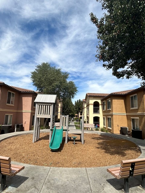 A playground with a green slide and wooden benches.