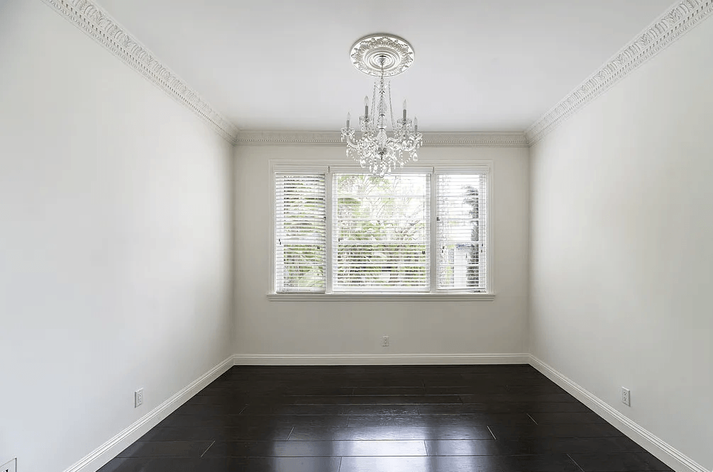 a dining room with white walls and a window with white shutters
