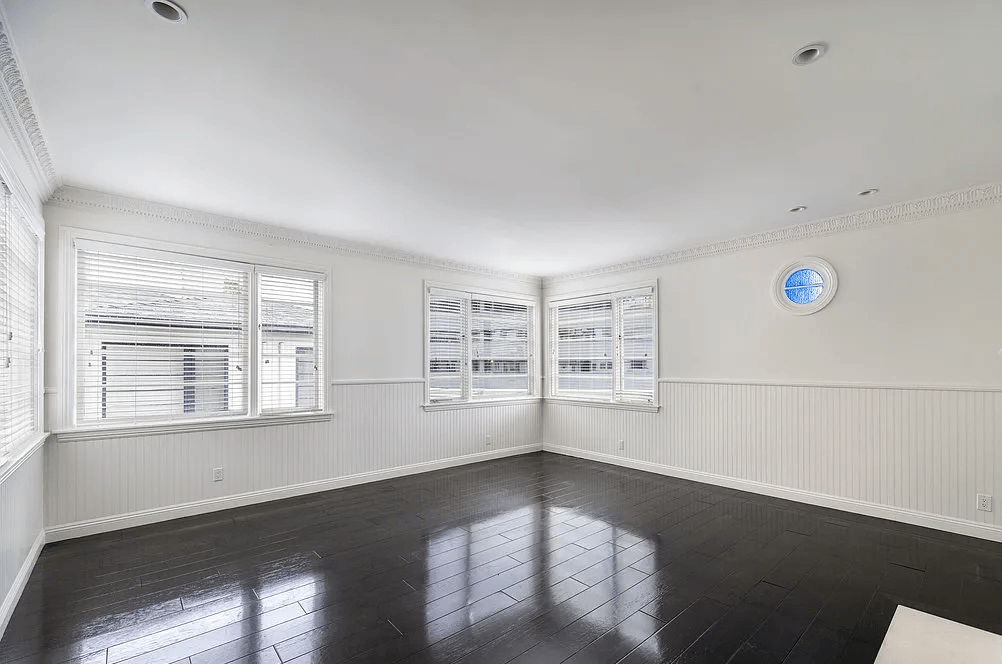 an empty room with three windows and a clock on the wall