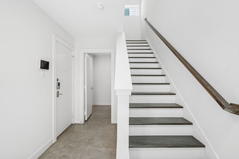 A staircase with a wooden handrail and white steps leads up to a white door.
