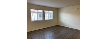 an empty living room with wood flooring and two windows