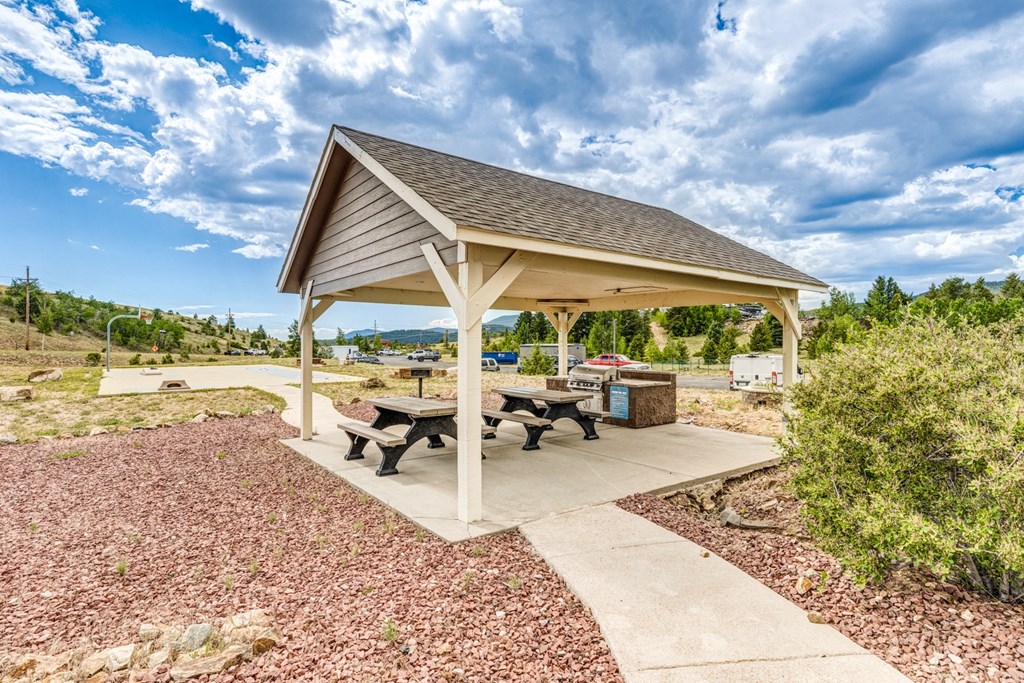 A pavilion with a picnic table is surrounded by gravel and a concrete walkway.
