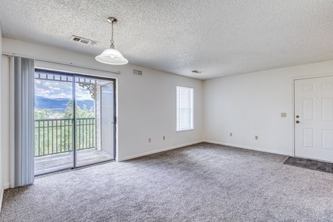 A spacious room with a sliding glass door leading to a balcony.