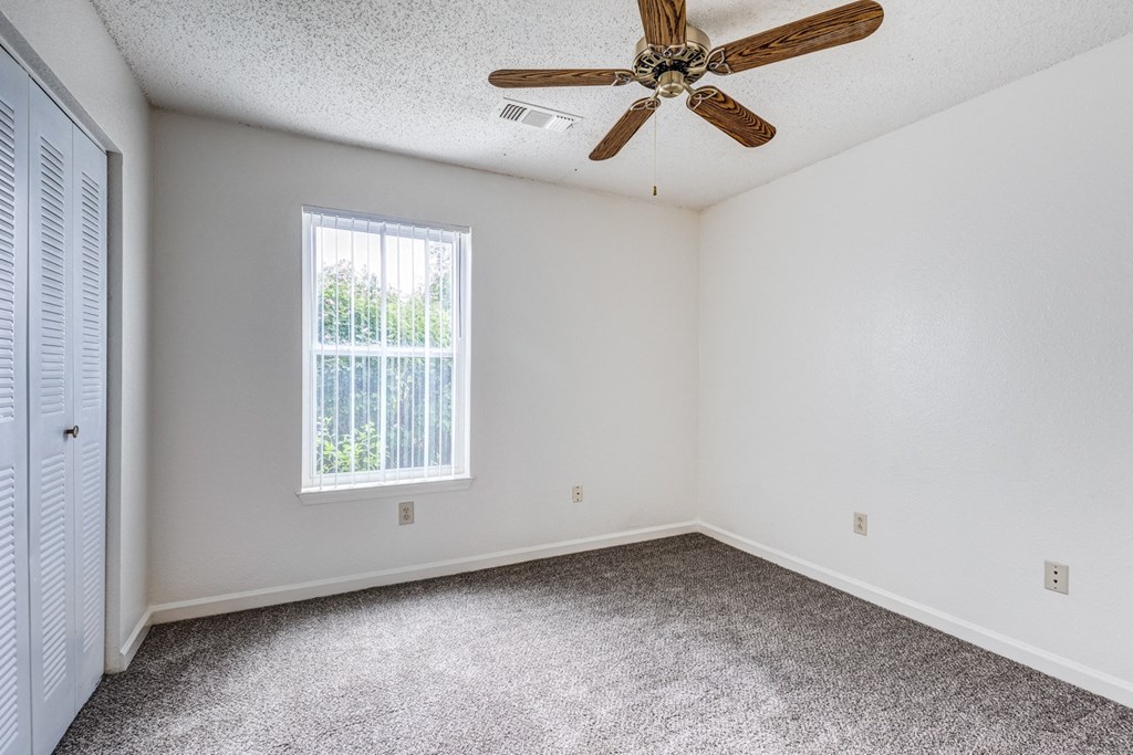 A room with a ceiling fan and a window with blinds.