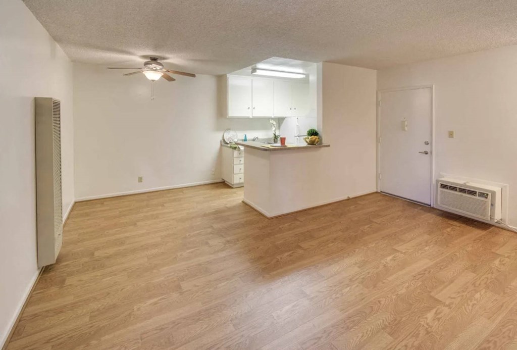 an empty living room with a kitchen and a ceiling fan
