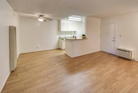 an empty living room with a kitchen and a ceiling fan