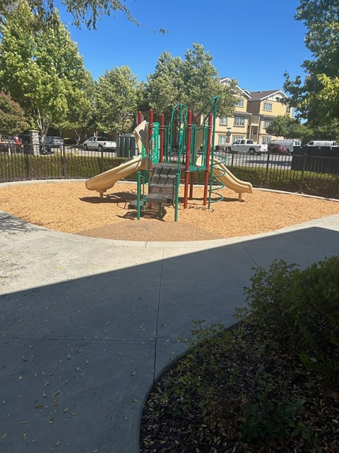 A playground with a green slide and a red and green swing set.