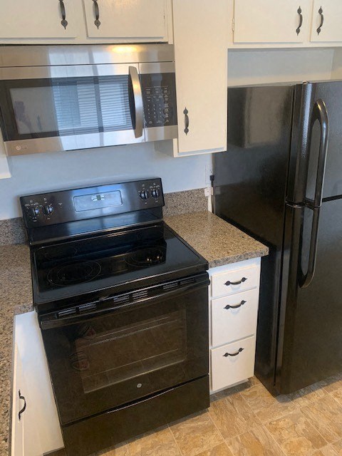 A black stove and oven in a kitchen with white cabinets.