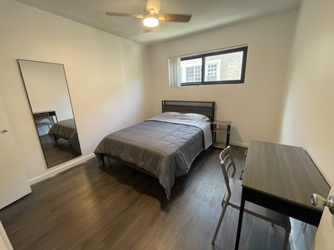 A bedroom with a bed, desk, and mirror.