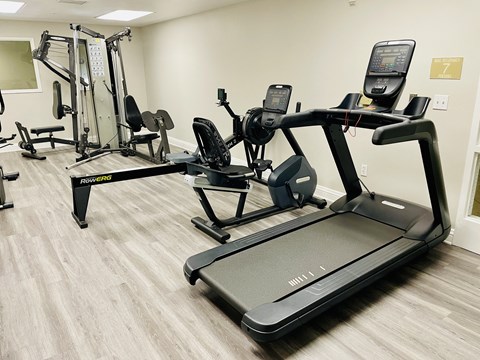 A treadmill is in the foreground of a well equipped gym.