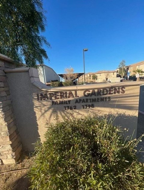A sign for Imperial Gardens Family Apartments stands in front of a building.
