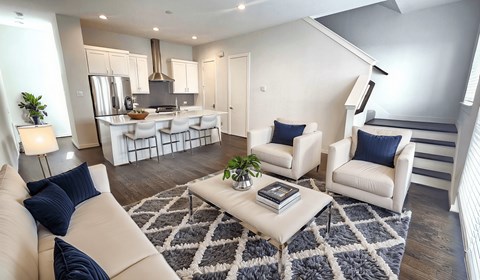 A modern living room with a kitchen area in the background.