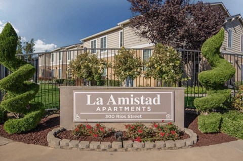 The image shows a sign for La Amistad Apartments with a building in the background.