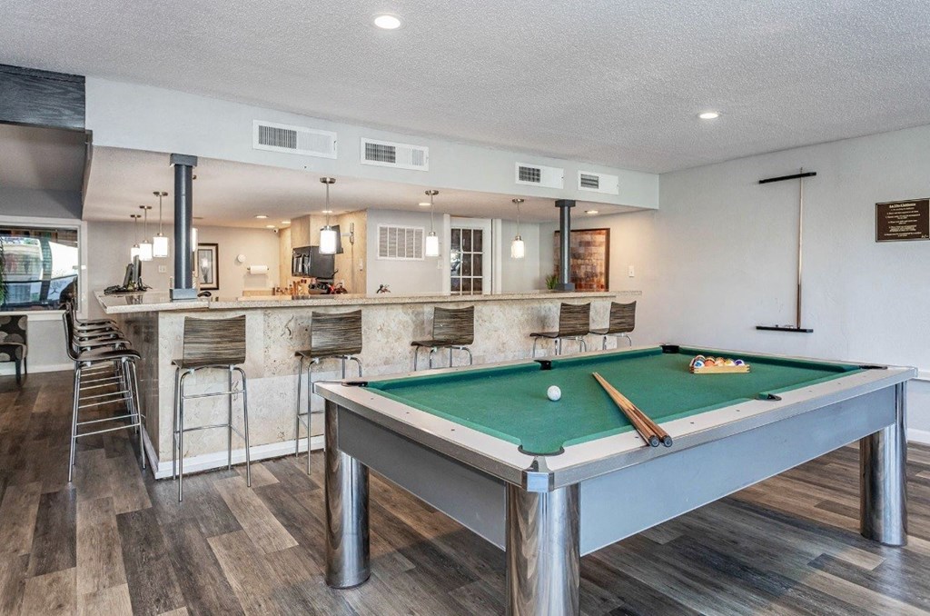 A pool table is in the middle of a room with a bar area.