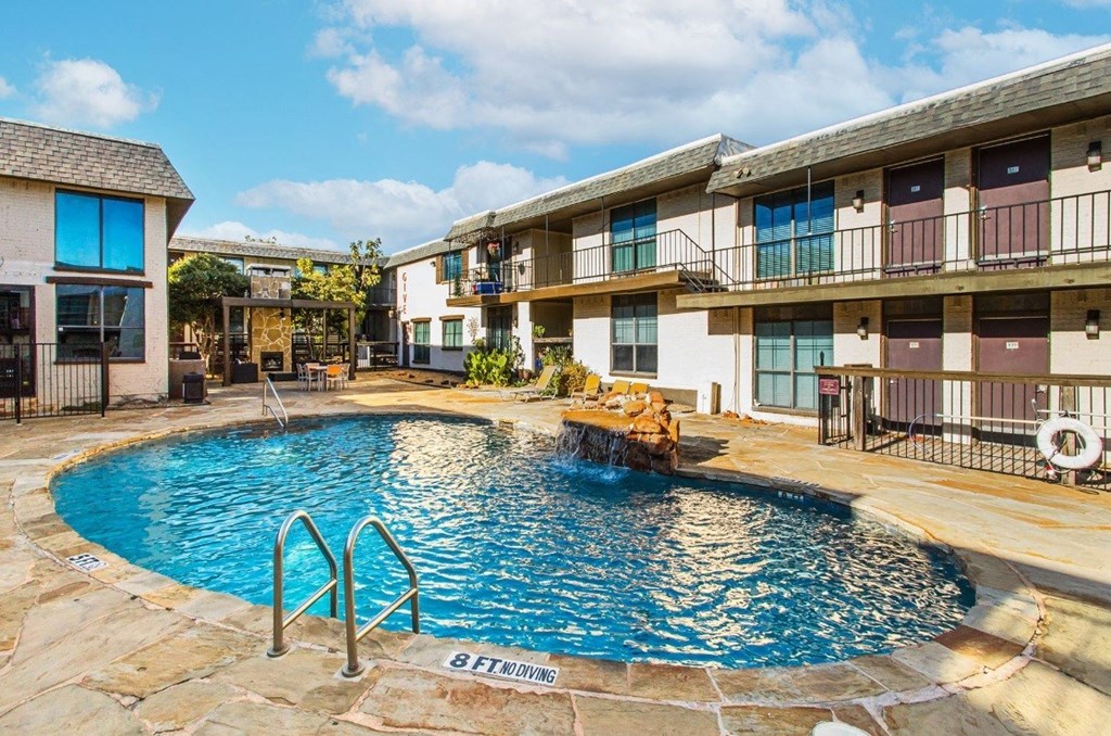 A swimming pool in front of a building with a stone border.
