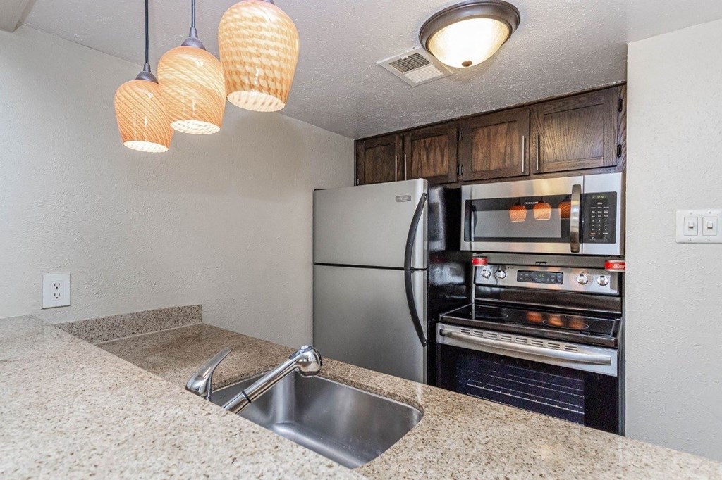 A kitchen with a stainless steel refrigerator and oven, a sink, and three hanging lights.