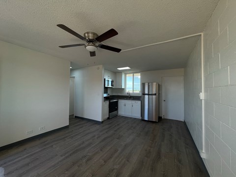 an empty living room with a ceiling fan and a kitchen
