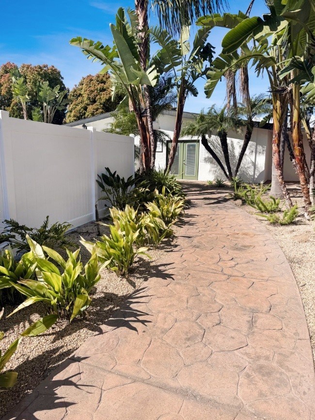 A white fence and a pathway with green plants on the sides.