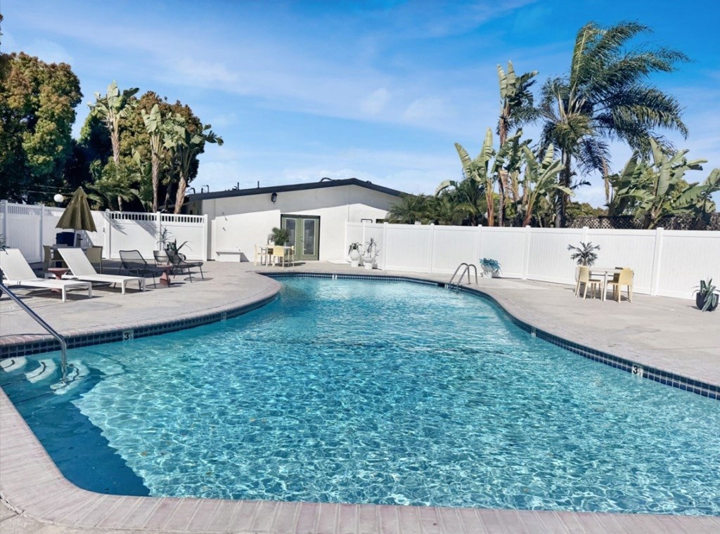 A large swimming pool surrounded by a white fence and palm trees.